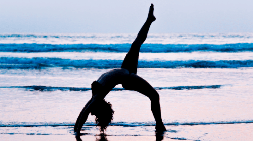 woman doing yoga backbend on beach featured