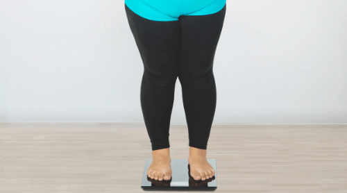 overweight woman in black and blue leggings standing on scale featured